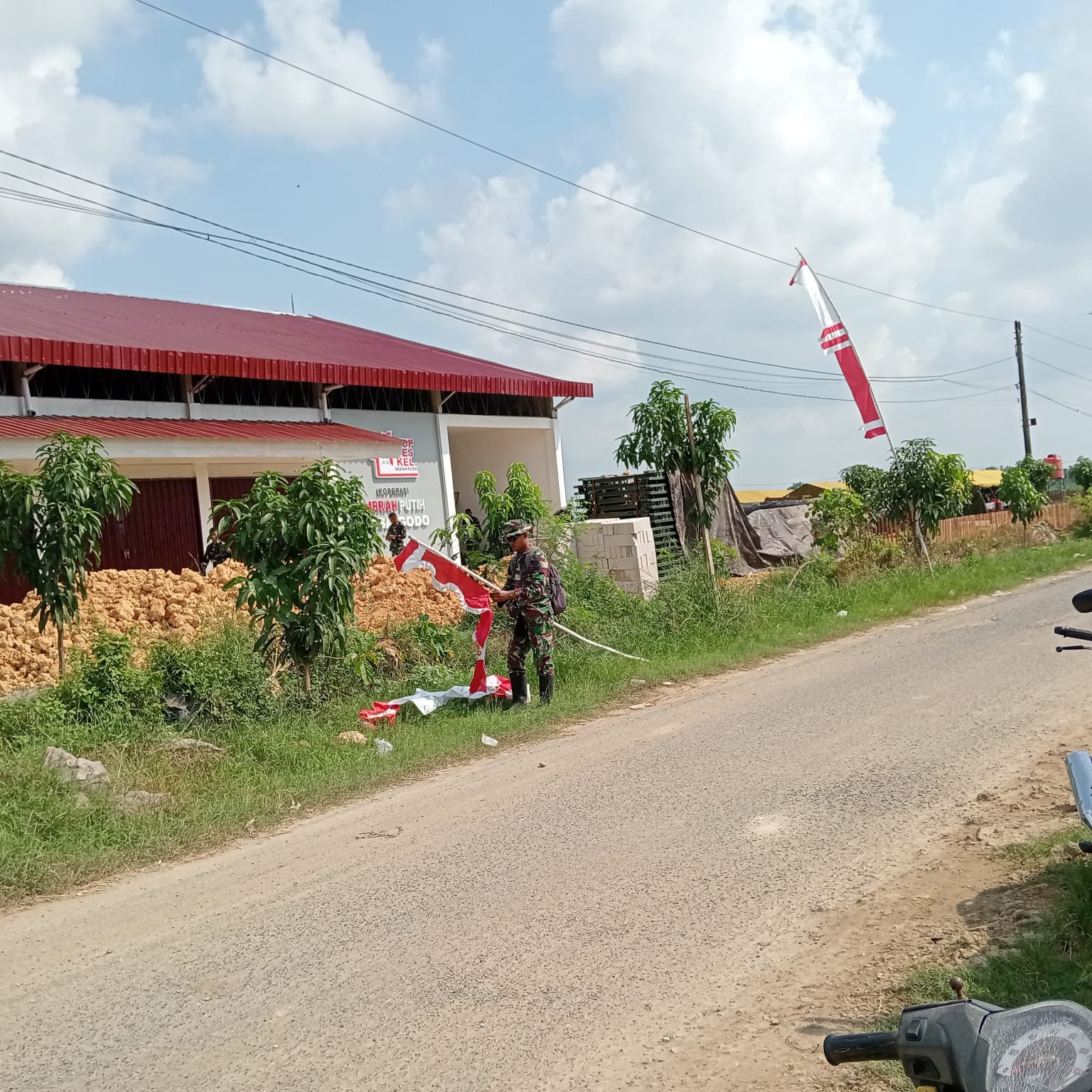 Persiapan Penutupan TMMD Reguler ke-128, Sertu Nursanto Pasang Umbul-Umbul di Lokasi Kegiatan